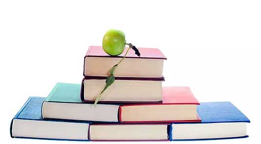 stack of colourful books with a green apple on top