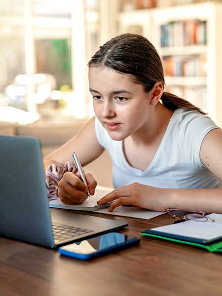 girl sitting in front of laptop taking notes